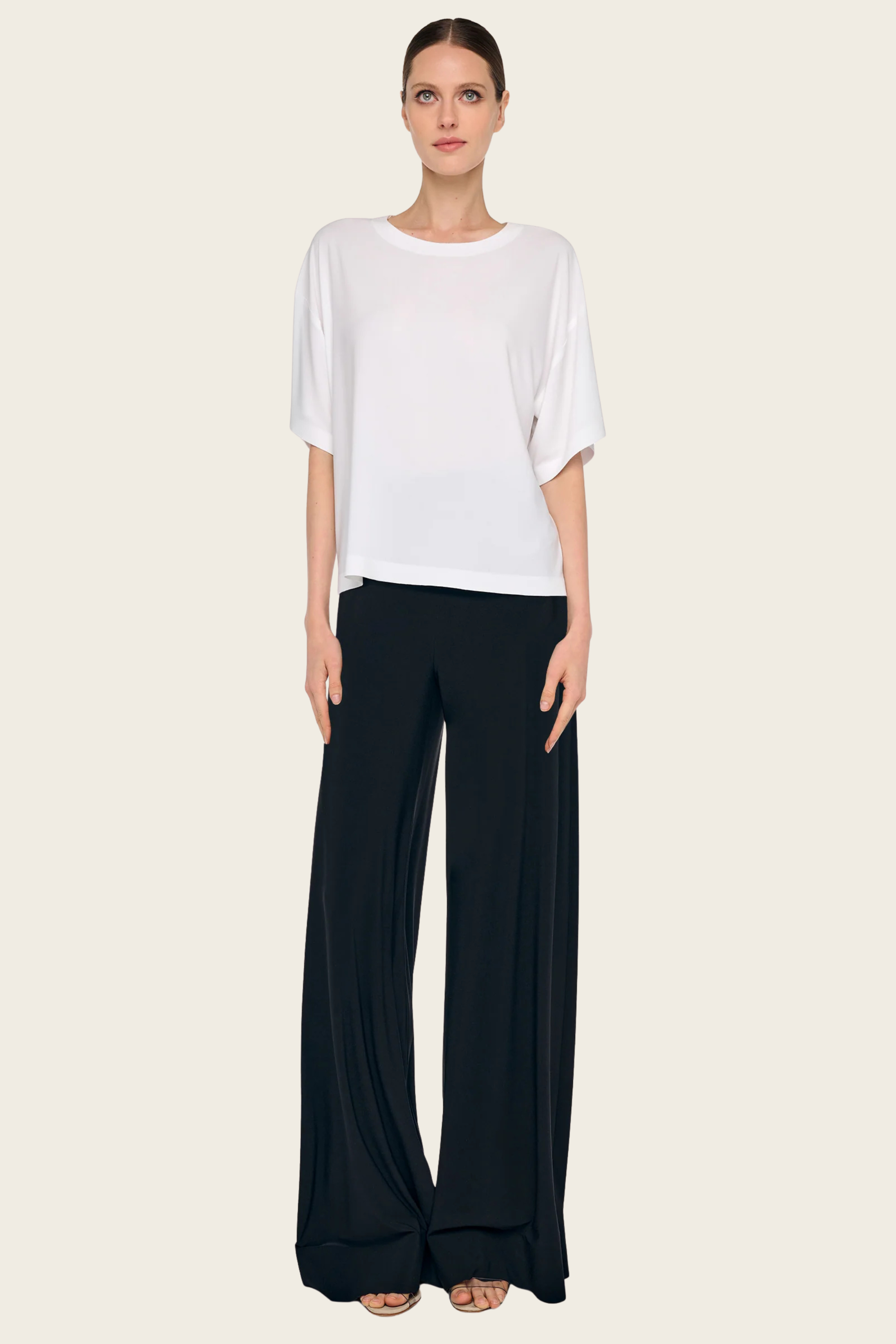 White short sleeve tee shirt by Norma Kamali styled with black flowing pants against a neutral background.