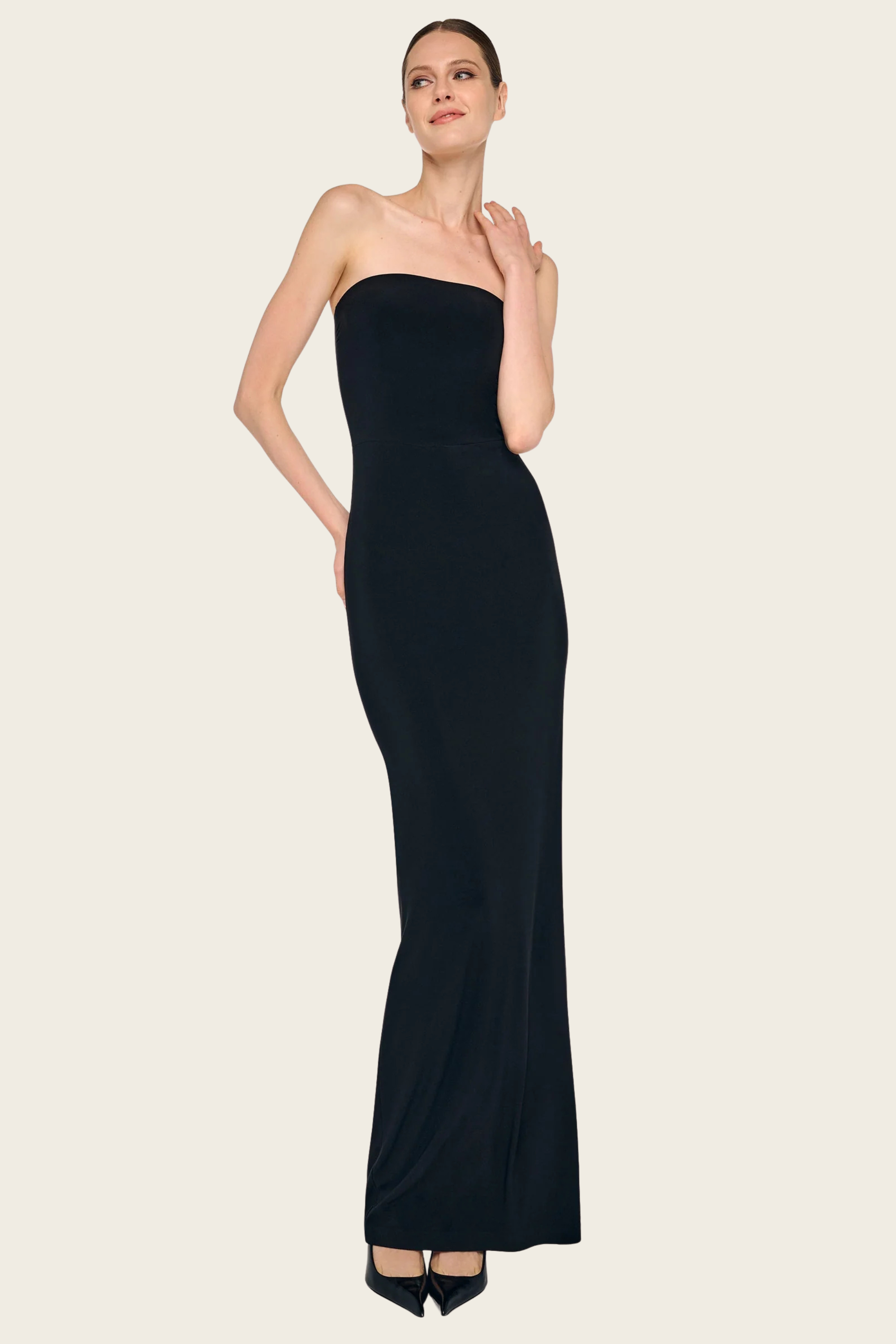 Black strapless long dress by Norma Kamali with fitted silhouette and black pumps.
